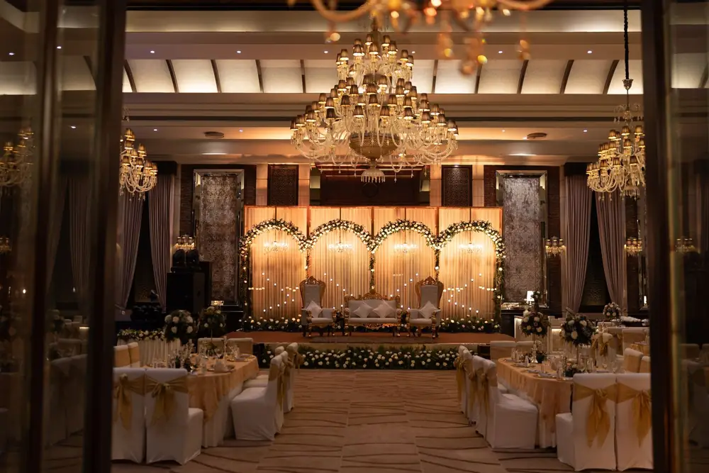 Grote feestzaal met podium, kroonluchters en gedekte tafels met gouden accenten